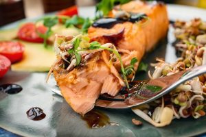 A Piece Of Baked Red Fish With A Side Dish Of Sprouts And Avocad