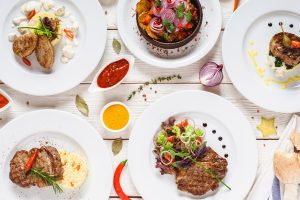 Food assortment top view. Buffet dishes selection on restaurant table. White plates with meals on white background flat lay.
